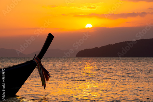 Silhouette Long Tail Boat in the tropical sea at golden sunset, mountains and orange sky with clouds