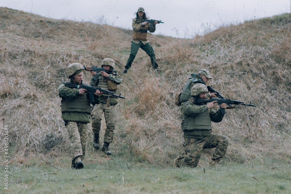 Team of five Ukrainian soldiers aims from kalashnikov assault rifles to russian enemy against background of hill.