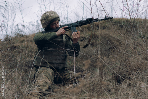 Ukrainian soldier aims from kalashnikov assault rifle to russian enemy.