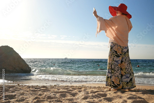 Summer vacation woman in red hat on the sea beach with mobile phone, woman blogger photo