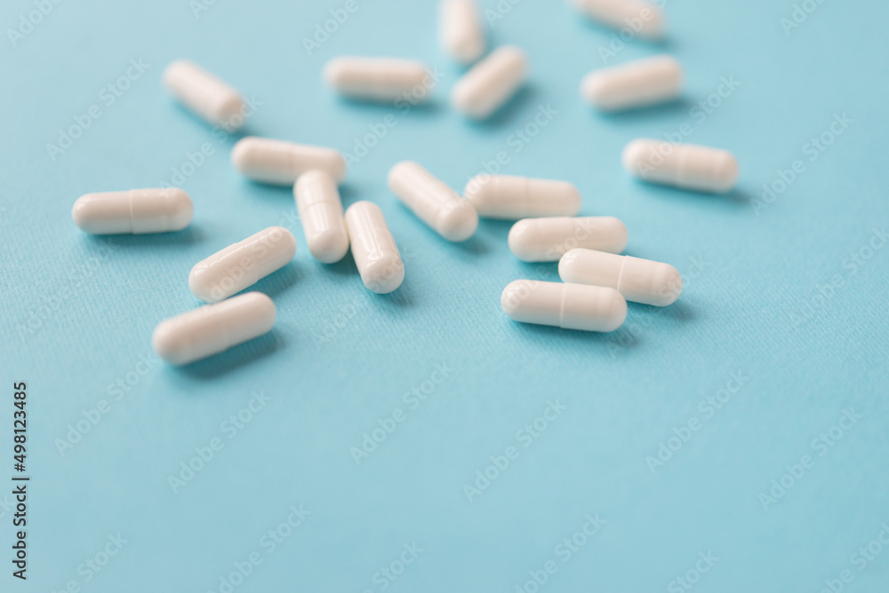 White capsule pills on a blue background. Medical background with copy space for text. White capsule pills on a blue background. Medical background with copy space for text.