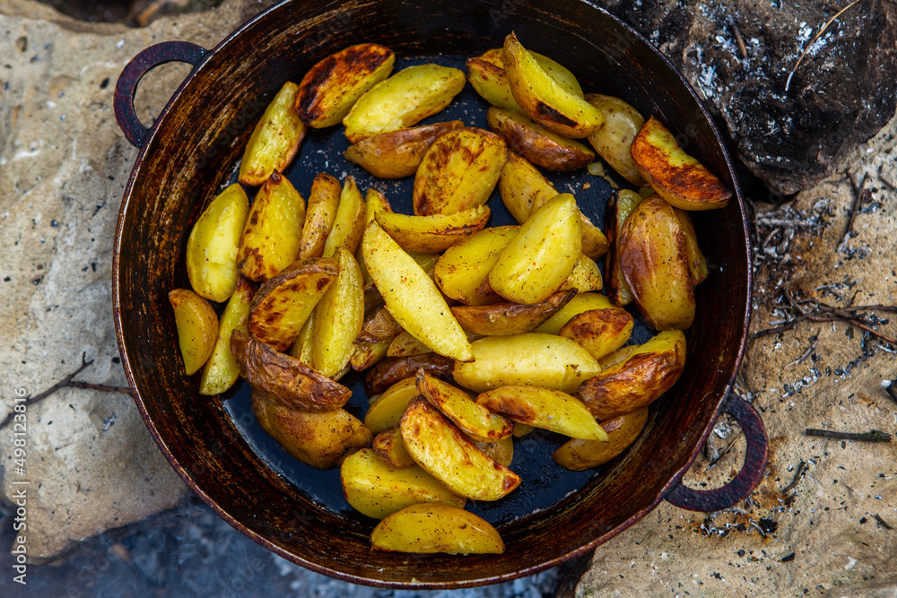 Homemade crispy potatoes on a frying pan on the fire outside. Picnic in nature with cooking. Homemade crispy potatoes on a frying pan on the fire outside. Picnic in nature with cooking.