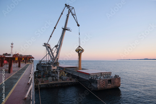 Transshipment of grain products from bulk carrier to the barge on Odessa, Ukraine anchorage during sunset