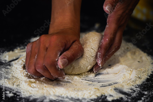 The cooking process of a bread dough. Baking bread recipe. Bakery breads food, detail view with woman hands working on dough at an old wood pan. flour falling on a dark table. detail.
