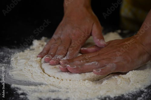 The cooking process of a bread dough. Baking bread recipe. Bakery breads food, detail view with woman hands working on dough at an old wood pan. flour falling on a dark table. detail.