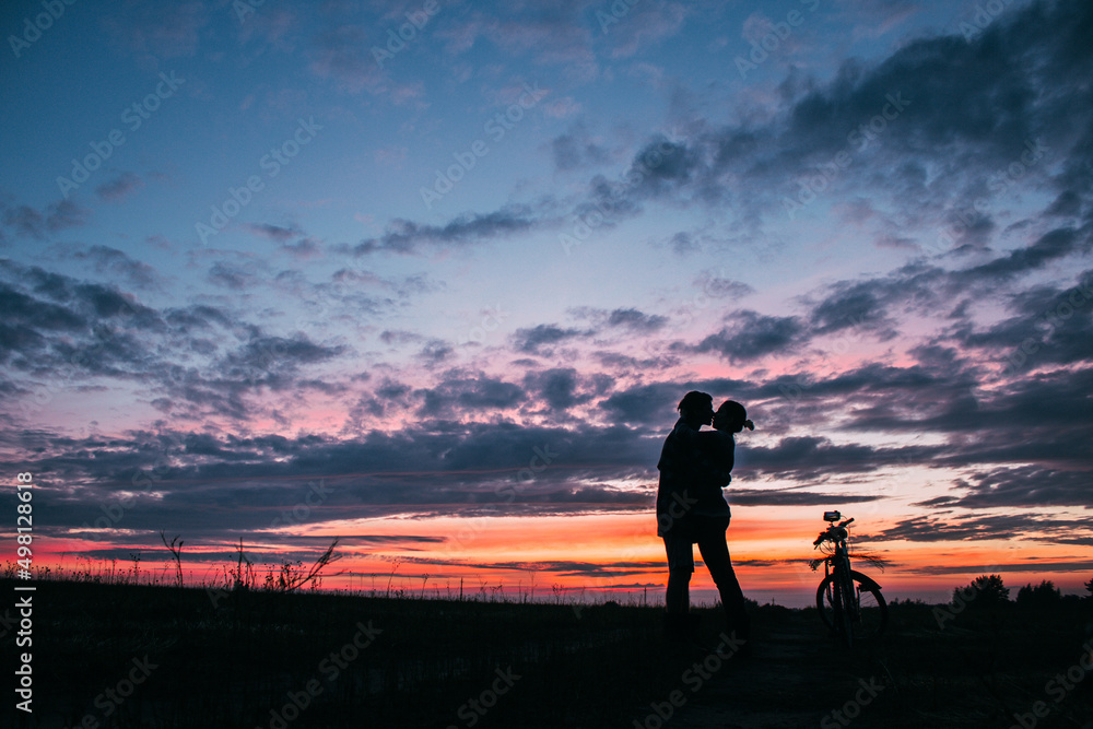 A couple kisses and hugs in a field at sunset, next to a bike