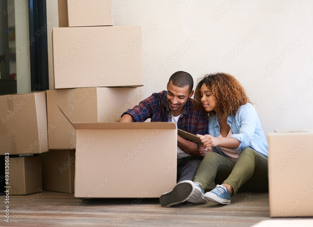 Whats in the box. Shot of a young couple unpacking a box together while sitting on the floor of their new home. Whats in the box. Shot of a young couple unpacking a box together while sitting on the floor of their new home.