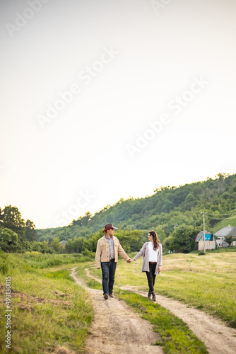 A Caucasian heterosexual couple walks down the alley, holding hands, near a picturesque village in Ukraine. Vertical photo.