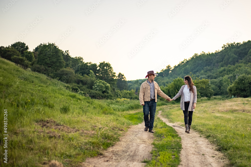 A Caucasian heterosexual couple walks down the alley, holding hands, near a picturesque village in Ukraine. A Caucasian heterosexual couple walks down the alley, holding hands, near a picturesque village in Ukraine.