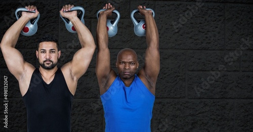 Two diverse fit men working out with dumbbells against copy space on grey brick wall background