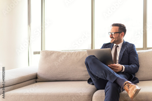 Confident cheerful manager sitting on sofa holding laptop © Route77