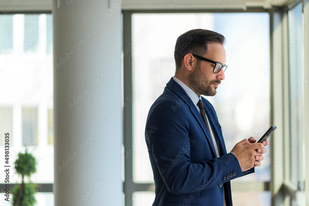 Young businessman standing next to window holding phone Young businessman standing next to window holding phone