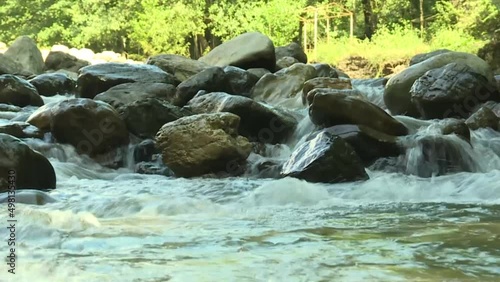 The rapid flow of water through the black stones on the river bank