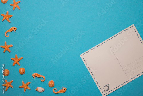 Turquoise background with postcard and seashells in the shape of starfish and seafood with empty space in the middle.