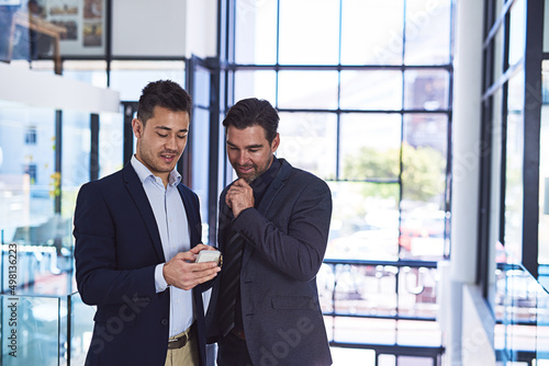 The client texted some great feedback on our latest deal.... Cropped shot of two businessmen discussing something on a cellphone in an office.