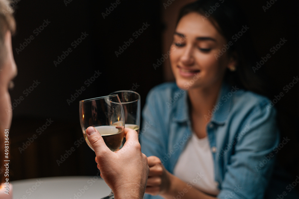 Close-up of happy young couple clinking glasses with wine sitting at table with candles in cozy dark room. Loving man and woman celebrating anniversary, Valentines day, enjoying romantic date. Close-up of happy young couple clinking glasses with wine sitting at table with candles in cozy dark room. Loving man and woman celebrating anniversary, Valentines day, enjoying romantic date.