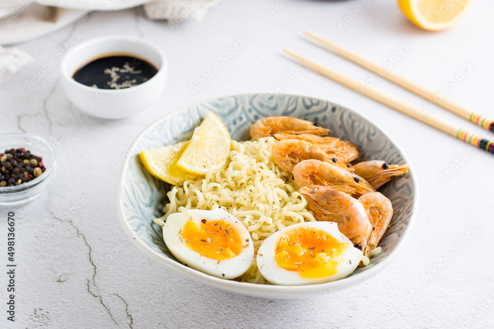 Chinese noodles with fried shrimp, boiled egg and lemon in a bowl on the table. Chinese noodles with fried shrimp, boiled egg and lemon in a bowl on the table.