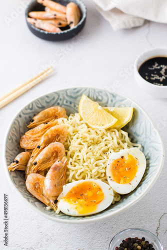 Chinese noodles with fried shrimp, boiled egg and lemon in a bowl close-up. Vertical view
