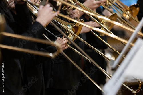 Many people playing the trombone during a performance with their trombone slides being in different positions