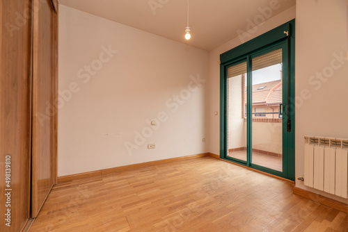 empty room with built-in wardrobe with sliding wooden doors, oak parquet floors, white aluminum radiator and exit to a terrace with green aluminum and glass doors