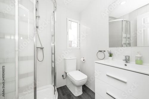 White bathroom with frameless wall mirror  white porcelain countertop sink to match wooden drawers and quarter circle shower stall
