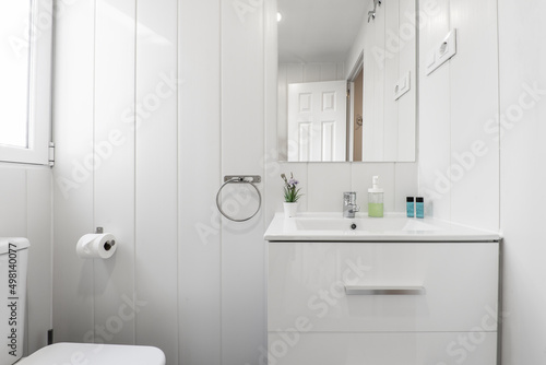 White bathroom with wall mounted frameless mirror  high gloss white wooden cabinet and aluminum window