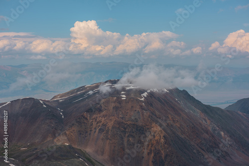 Atmospheric mountain landscape with low cloud on high mountain top with snow under cloudy sky. Dramatic aerial view to large rocky mountain peak with low clouds. Beautiful view from above to pinnacle.