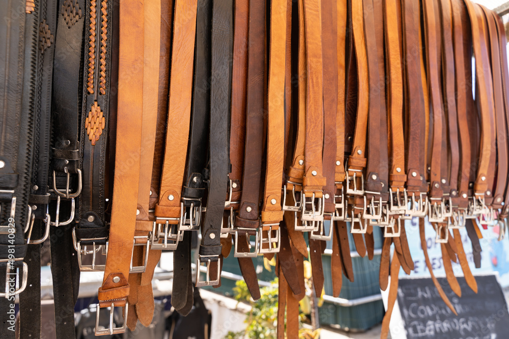 Brown and black leather belts hanging on street market stall. Handmade accessories concept