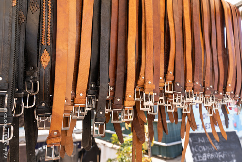 Brown and black leather belts hanging on street market stall. Handmade accessories concept