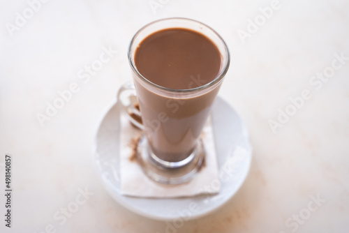 Hot chocolate milk glass on small plate from top. Sweet drink on white table