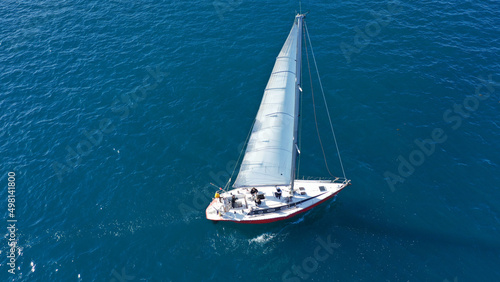 Aerial drone photo of beautiful sail boat with white sails cruising deep blue Aegean sea