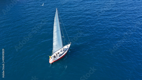Aerial drone photo of beautiful sail boat with white sails cruising deep blue Aegean sea