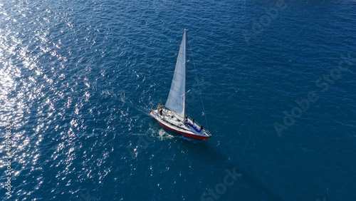 Aerial drone photo of beautiful sail boat with white sails cruising deep blue Aegean sea © aerial-drone