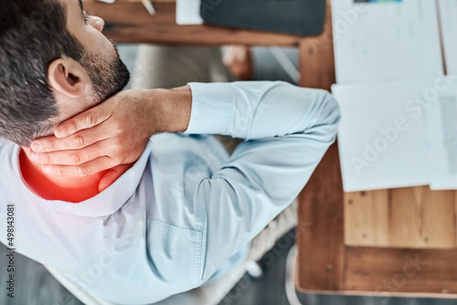 The day has turned into a real pain in the neck. High angle shot of a young businessman suffering with neck pain while working in an office. photo