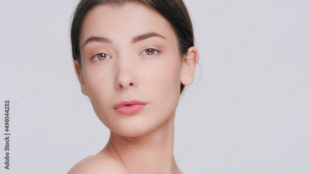 Extreme close-up beauty portrait of young dark-haired woman slowly looks up at camera and turns a bit against grey seamless studio background | beauty products commercial concept. Extreme close-up beauty portrait of young dark-haired woman slowly looks up at camera and turns a bit against grey seamless studio background | beauty products commercial concept.
