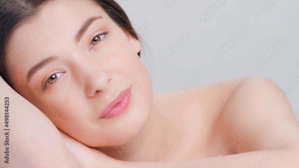 Close-up beauty portrait of young attractive woman lays her head on her hands and looks at camera on grey background | beauty products advertising concept Close-up beauty portrait of young attractive woman lays her head on her hands and looks at camera on grey background | beauty products advertising concept