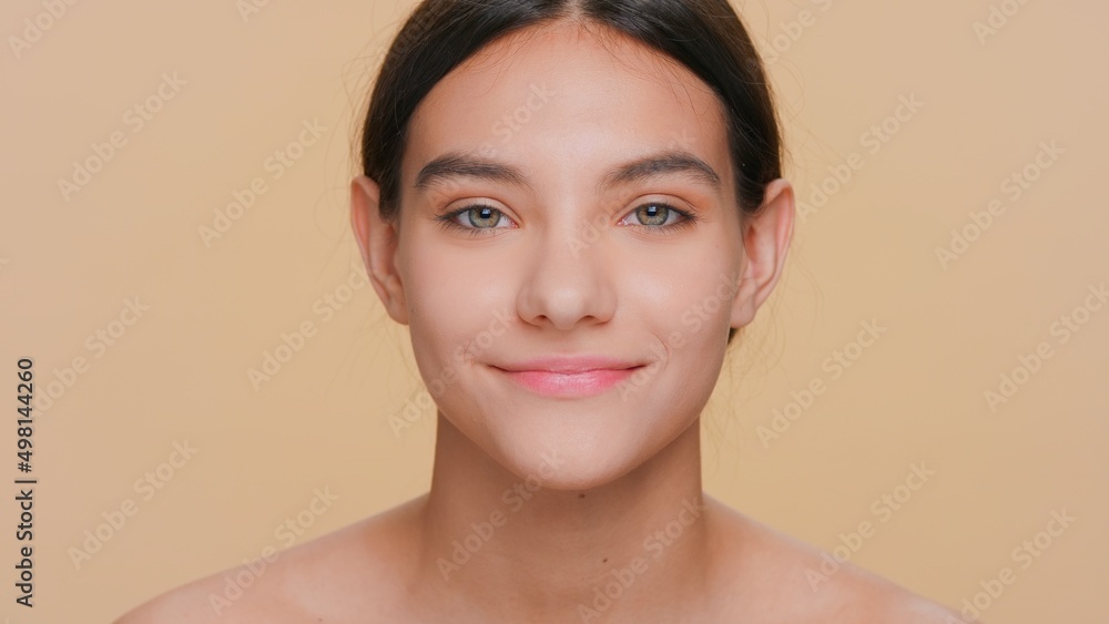 Close-up beauty portrait of young positive dark-haired woman looks at camera against beigt background Close-up beauty portrait of young positive dark-haired woman looks at camera against beigt background
