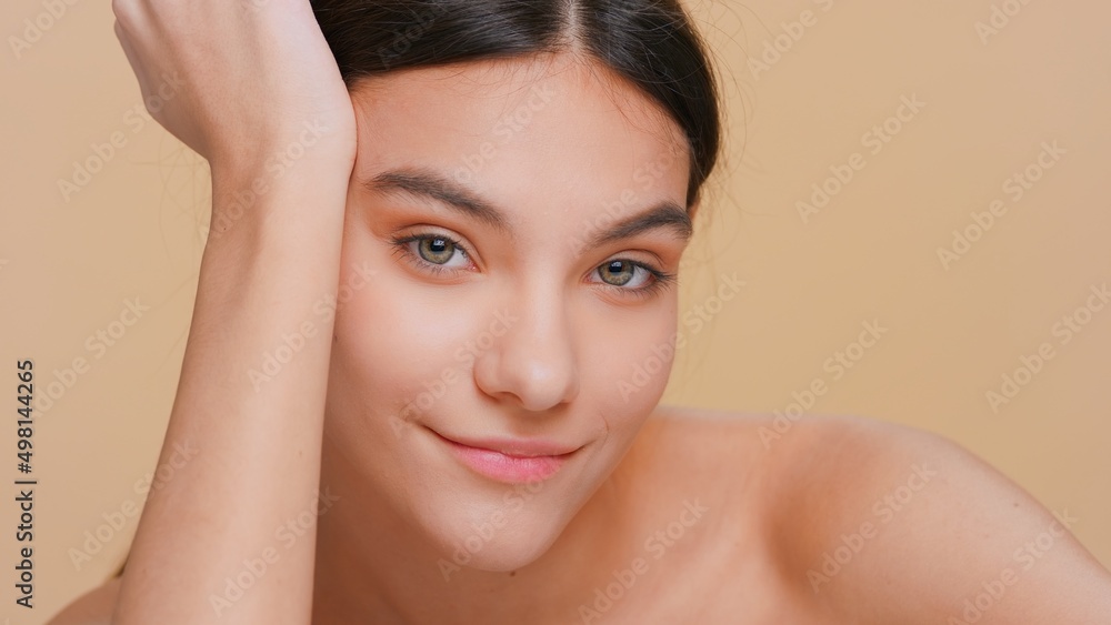 Close-up beauty portrait of young brunette woman with pure skin props her head up with her hand on beige background | Skin care products promotion concept Close-up beauty portrait of young brunette woman with pure skin props her head up with her hand on beige background | Skin care products promotion concept