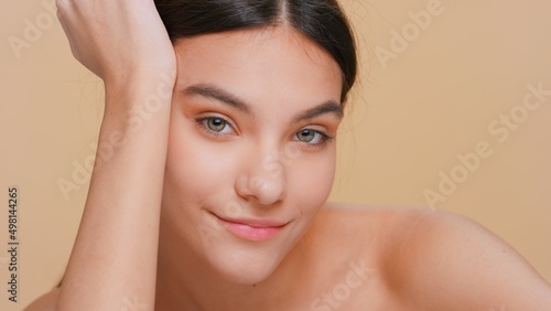 Close-up beauty portrait of young brunette woman with pure skin props her head up with her hand on beige background | Skin care products promotion concept