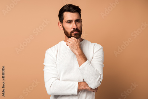 Thoughtful brunette man with beard in white t-shirt holding his chin and pondering