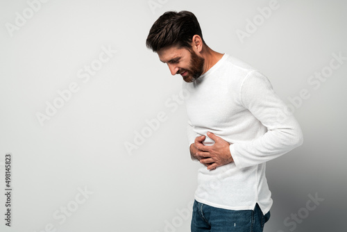 Bearded man standing and holding his painful belly, feeling bad, photo
