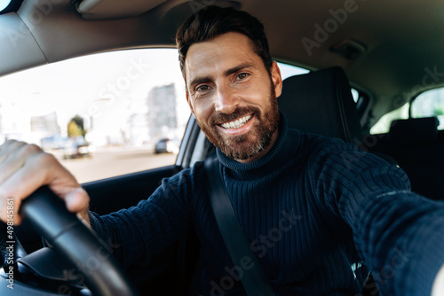 Handsome bearded man holding camera and making selfie while sitting in the car
