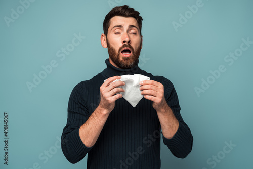 Unhealthy flu-sick man sneezing loudly in tissue, feeling unwell with runny nose