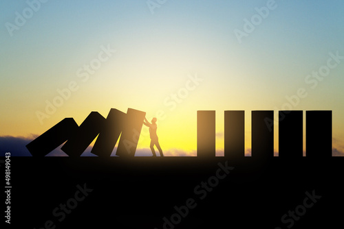 Backlit business man stopping abstract wooden domino blocks on bright sunset sky background with mock up place. Crisis, recession and challenge concept. photo