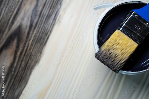 Copy space with paint brush on can lying on wooden background. Close-up paintbrush with liquid dark brown paint on the brush. Painting tools on wooden surface. Top view. Copyspace. Vintage style.