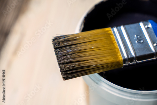 Copy space with paint brush on can lying on wooden background. Close-up paintbrush with liquid dark brown paint on the brush. Painting tools on wooden surface. Top view. Copyspace. Vintage style.