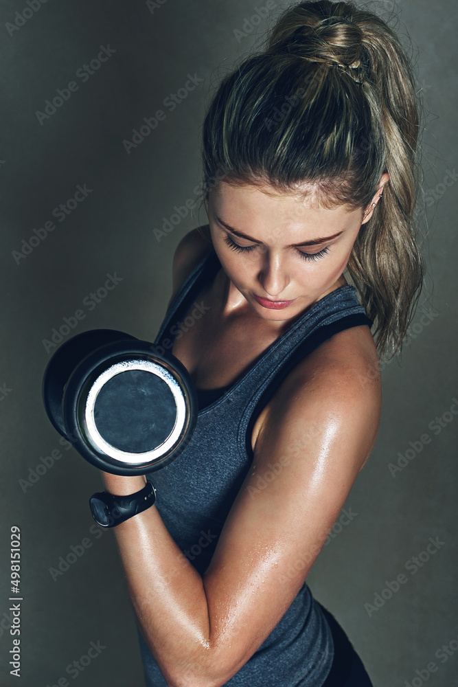 Fototapeta premium Strength is something you choose. Shot of a young woman lifting dumbbells against a gray background.