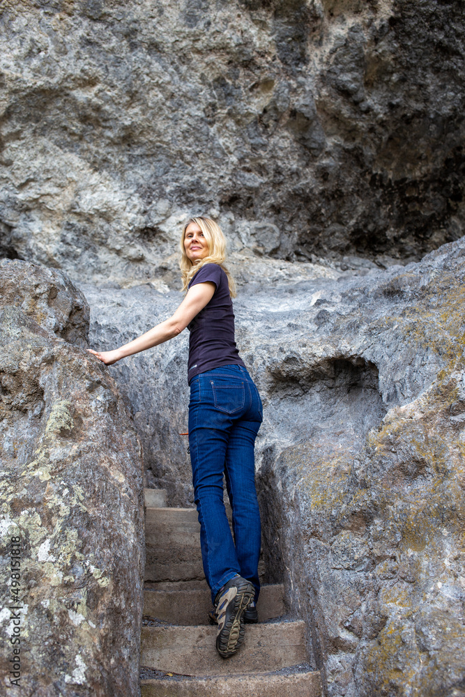 Attractive Blonde Woman Hiking Between Rocks on a Cliff Walk and Looking Back at Us
