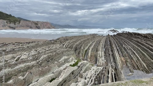 Rough sea waves breaking on sharp limestone rock layers in Zumaia beach on cloudy day. Popular flysch landmark in the Basque Country