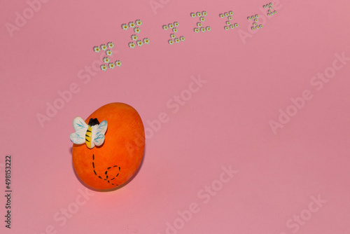 a bee moving around an orange egg and a zzzzz of flowers with copy space photo